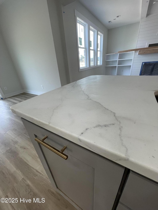 kitchen featuring gray cabinetry, a fireplace, light wood-style flooring, and light stone countertops