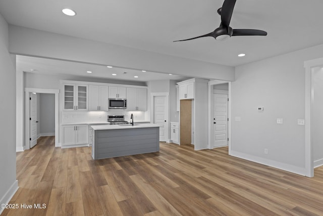 kitchen with stainless steel appliances, a center island with sink, white cabinets, and light wood-type flooring