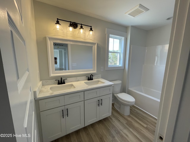 bathroom with toilet, wood finished floors, a sink, and visible vents