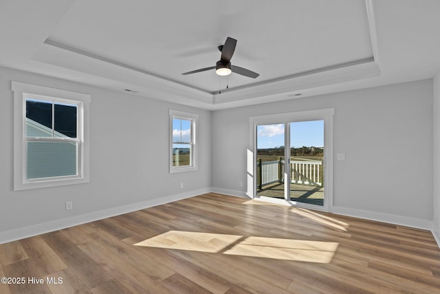 spare room featuring a tray ceiling, visible vents, ceiling fan, light wood-type flooring, and baseboards