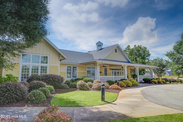 view of front of home with a shingled roof, a ceiling fan, a front lawn, and board and batten siding