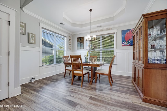 dining area with a chandelier, a decorative wall, wood finished floors, visible vents, and a raised ceiling