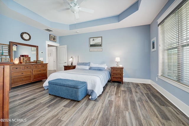 bedroom featuring visible vents, baseboards, a ceiling fan, a raised ceiling, and wood finished floors