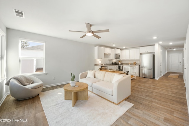 living room featuring visible vents, baseboards, a ceiling fan, light wood-style flooring, and recessed lighting