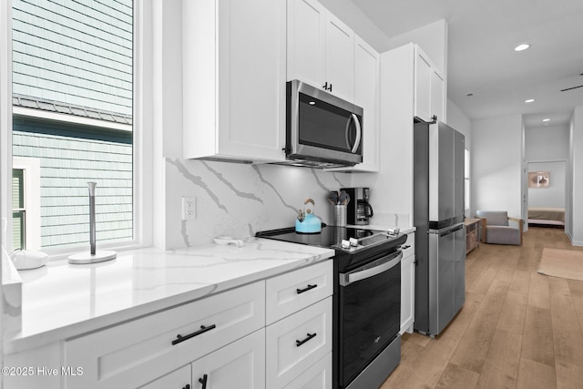 kitchen with light stone counters, light hardwood / wood-style flooring, white cabinets, and appliances with stainless steel finishes