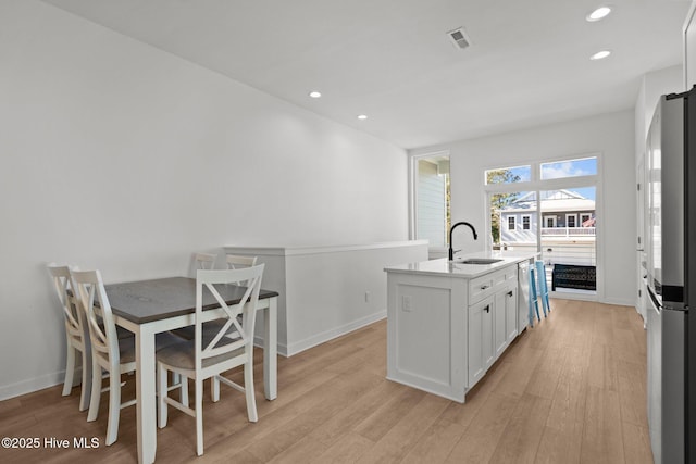 kitchen featuring sink, light wood-type flooring, stainless steel appliances, a kitchen island with sink, and white cabinets