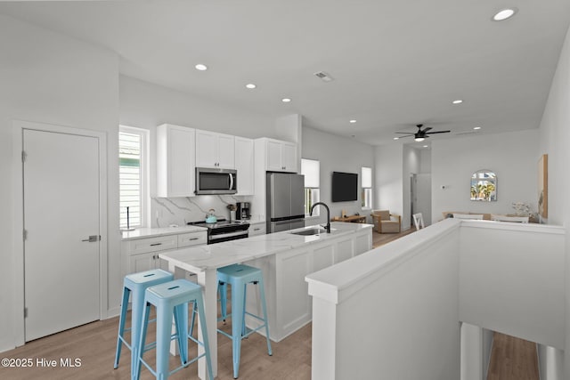 kitchen featuring appliances with stainless steel finishes, a center island with sink, white cabinets, and a kitchen breakfast bar