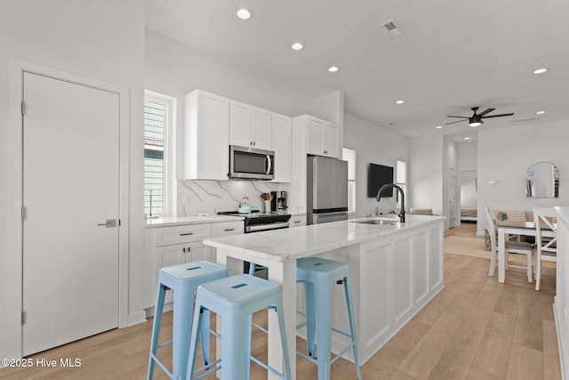 kitchen featuring a breakfast bar, sink, an island with sink, stainless steel appliances, and white cabinets