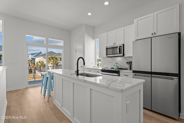 kitchen featuring an island with sink, sink, white cabinets, stainless steel appliances, and light stone countertops