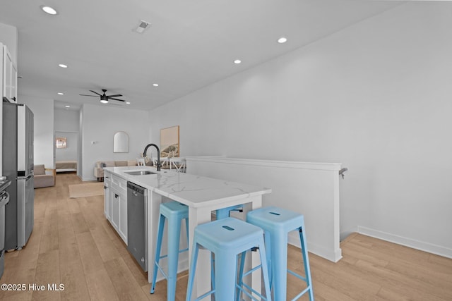 kitchen with light stone countertops, an island with sink, white cabinets, and appliances with stainless steel finishes