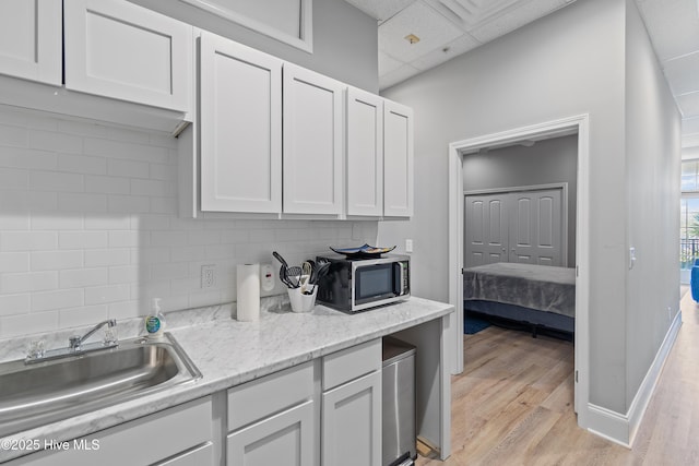 kitchen with backsplash, sink, white cabinets, and light wood-type flooring