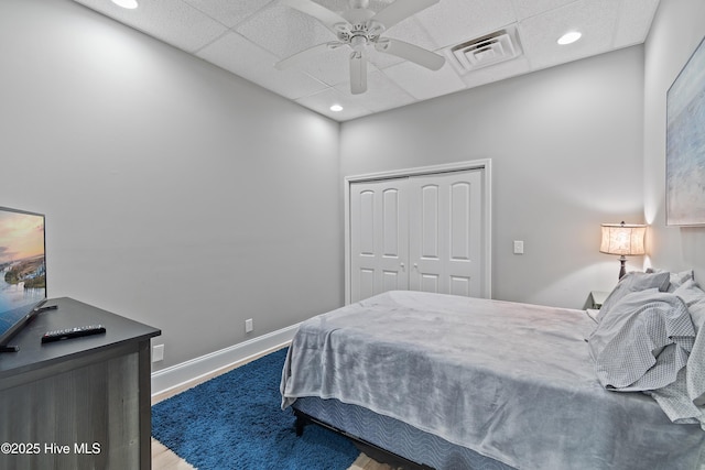 bedroom featuring hardwood / wood-style flooring, ceiling fan, a closet, and a drop ceiling