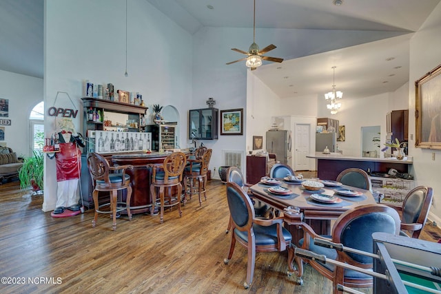 dining room featuring bar, ceiling fan with notable chandelier, wood-type flooring, and high vaulted ceiling