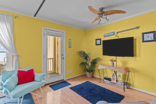 living area with ceiling fan, ornamental molding, a textured ceiling, and light wood-type flooring