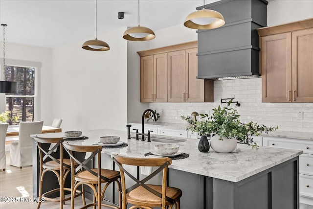 kitchen with pendant lighting, a kitchen island with sink, sink, and decorative backsplash