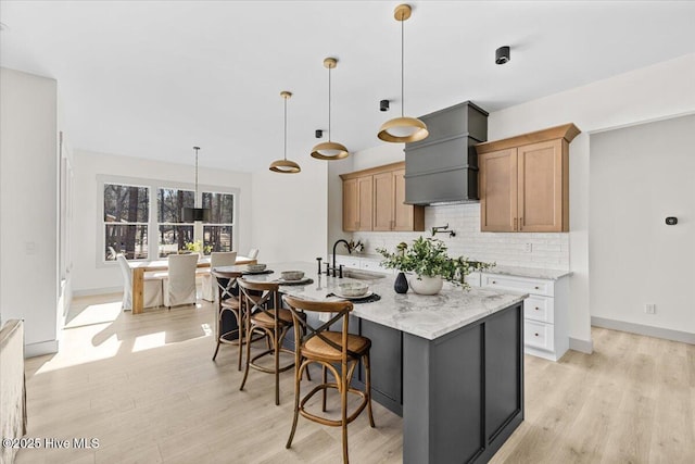 kitchen with light stone counters, decorative light fixtures, custom range hood, and a spacious island