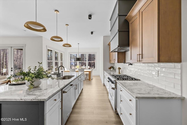 kitchen with decorative light fixtures, sink, white cabinets, light stone counters, and stainless steel appliances