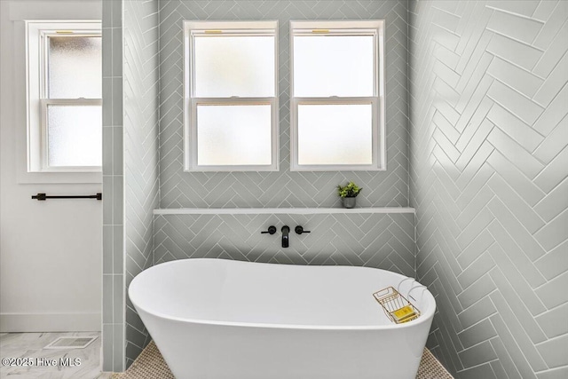 bathroom featuring a bath, tile walls, and a wealth of natural light