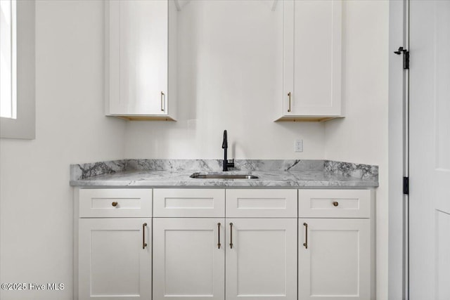 kitchen with light stone countertops, sink, and white cabinets