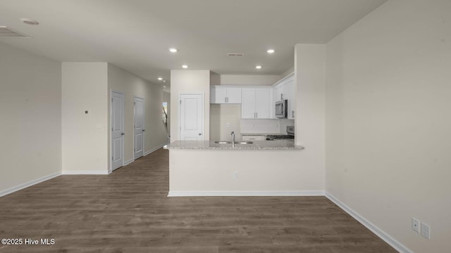 kitchen featuring a peninsula, a sink, white cabinets, appliances with stainless steel finishes, and dark wood-style floors