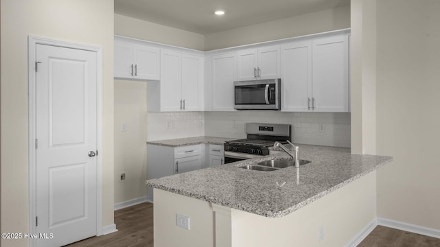 kitchen with a peninsula, white cabinetry, appliances with stainless steel finishes, light stone countertops, and dark wood finished floors