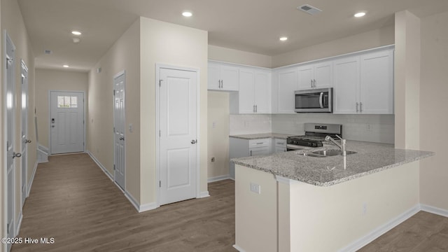 kitchen featuring light stone counters, stainless steel appliances, a peninsula, wood finished floors, and visible vents