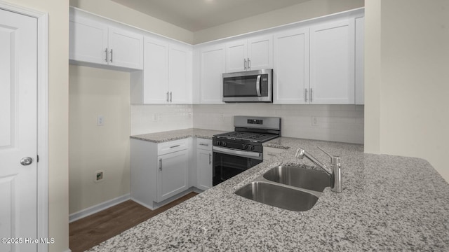 kitchen with appliances with stainless steel finishes, a sink, white cabinetry, and light stone countertops