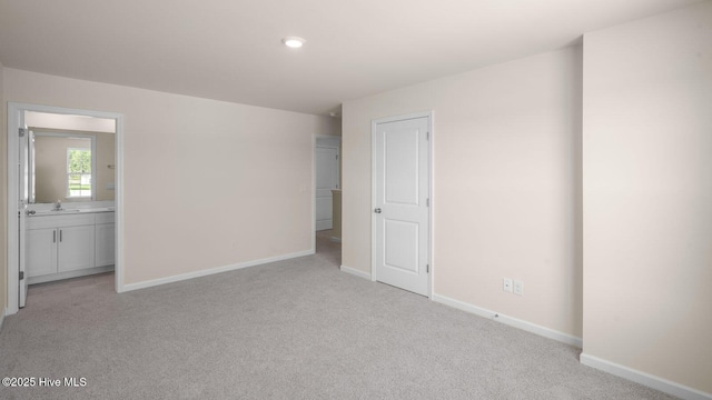 unfurnished bedroom with light carpet, ensuite bath, a sink, and baseboards