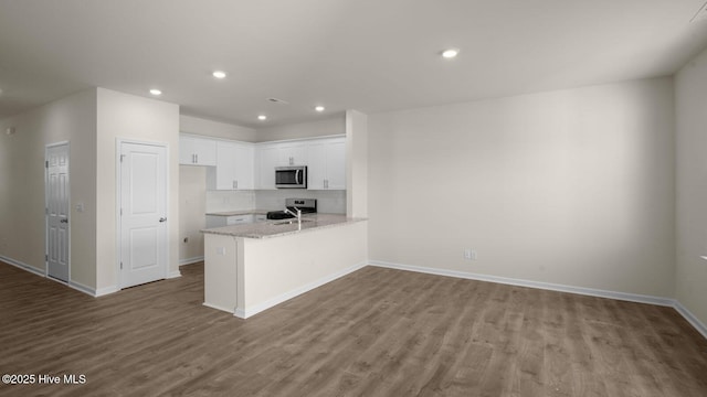 kitchen with baseboards, white cabinets, stainless steel microwave, wood finished floors, and a peninsula