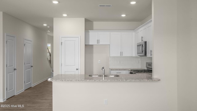 kitchen with a peninsula, light stone countertops, stainless steel appliances, white cabinetry, and a sink