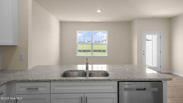 kitchen with dishwasher, light stone counters, wood finished floors, white cabinetry, and a sink