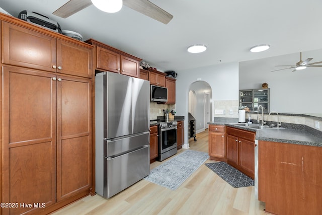 kitchen featuring sink, ceiling fan, stainless steel appliances, light hardwood / wood-style floors, and decorative backsplash