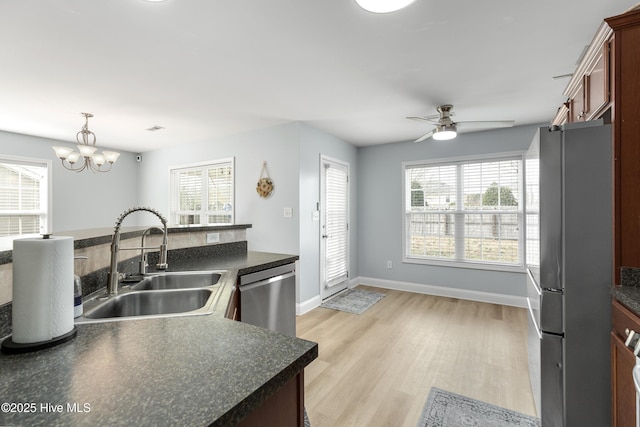 kitchen featuring sink, decorative light fixtures, light hardwood / wood-style floors, stainless steel appliances, and ceiling fan with notable chandelier