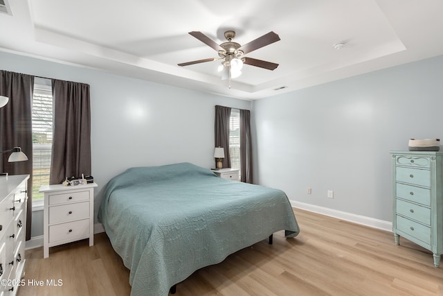 bedroom with ceiling fan, a raised ceiling, and light hardwood / wood-style flooring