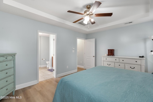 bedroom featuring ensuite bathroom, ceiling fan, light wood-type flooring, and a tray ceiling