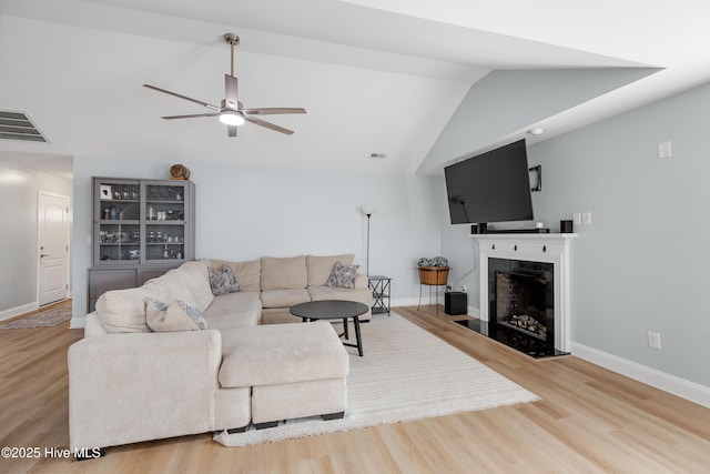 living room with ceiling fan, a fireplace, vaulted ceiling, and light hardwood / wood-style flooring