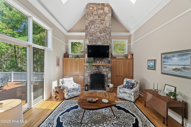 living room featuring a stone fireplace, high vaulted ceiling, light hardwood / wood-style floors, and a skylight