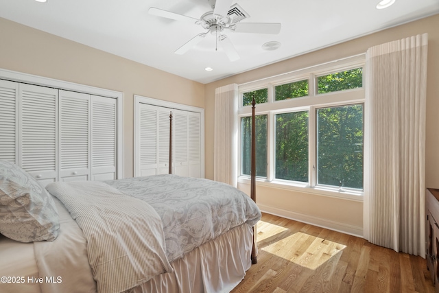 bedroom featuring ceiling fan, light hardwood / wood-style flooring, and two closets