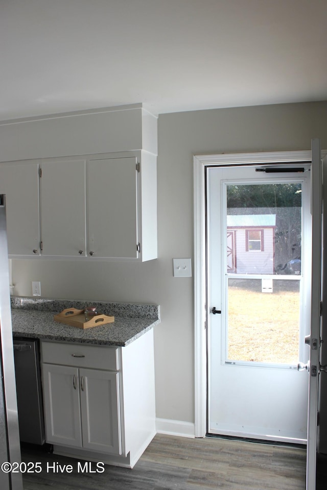 kitchen with dark wood-type flooring, stainless steel dishwasher, white cabinets, and dark stone counters