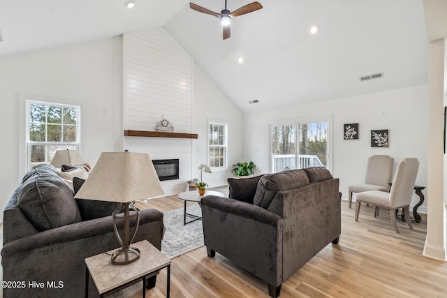 living room with ceiling fan, high vaulted ceiling, a fireplace, and light wood-type flooring