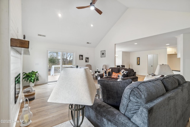 living room featuring high vaulted ceiling, a fireplace, light hardwood / wood-style floors, and ceiling fan