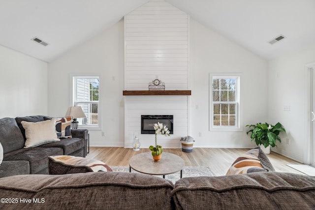 living room featuring high vaulted ceiling, a fireplace, and light hardwood / wood-style floors