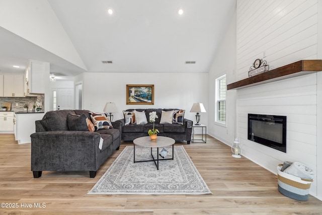 living room featuring sink, a fireplace, light hardwood / wood-style floors, and high vaulted ceiling