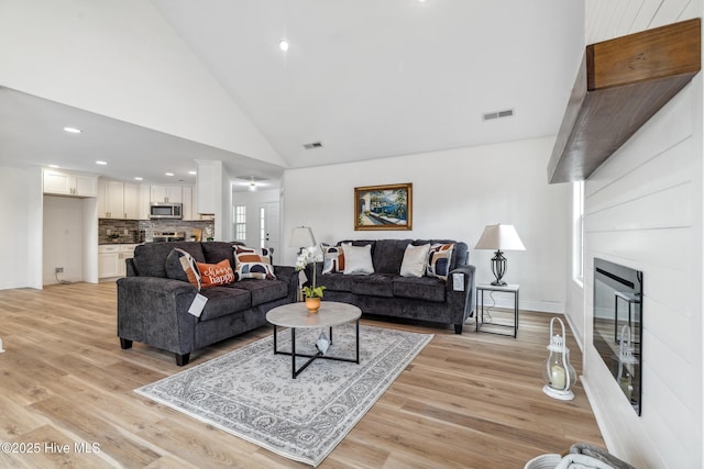 living room featuring a fireplace, a wealth of natural light, high vaulted ceiling, and light wood-type flooring