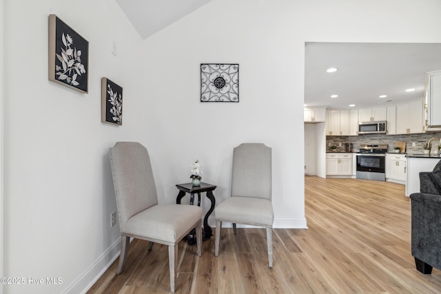 sitting room featuring sink, vaulted ceiling, and light wood-type flooring