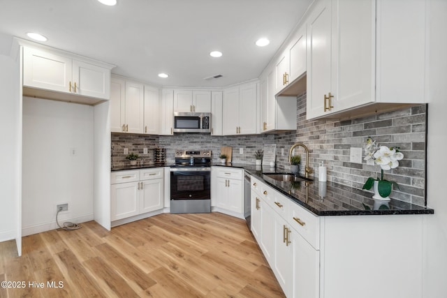 kitchen with white cabinetry, appliances with stainless steel finishes, sink, and dark stone counters