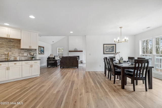 dining area featuring vaulted ceiling, sink, a fireplace, and light hardwood / wood-style floors