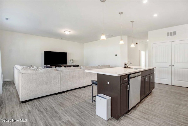 kitchen featuring sink, dishwasher, a kitchen island with sink, decorative light fixtures, and light wood-type flooring