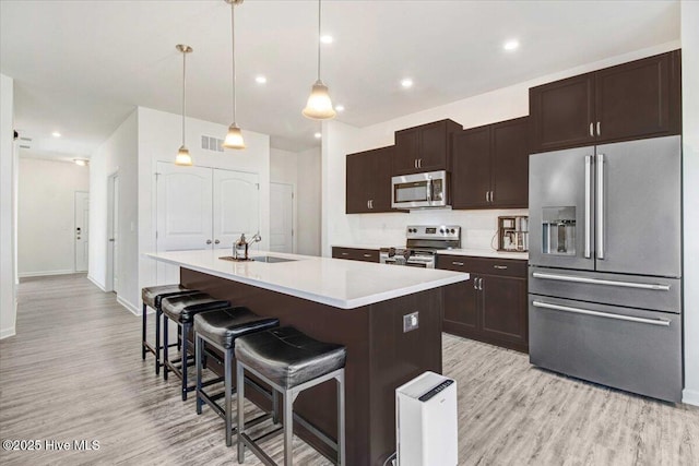 kitchen featuring sink, a breakfast bar area, stainless steel appliances, a center island with sink, and decorative light fixtures