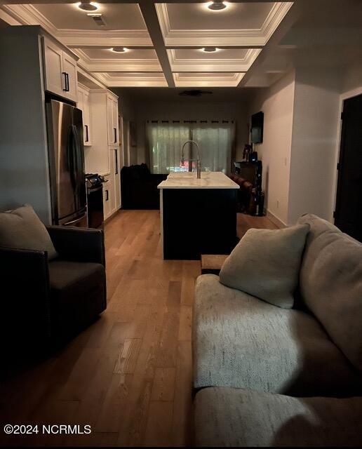 kitchen with white cabinetry, wood-type flooring, refrigerator, and a center island with sink